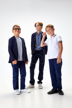 Photo for Children, boys, classmates in stylish school uniform and glasses standing against white studio background. Emotions. Concept of childhood, school, education, fashion, style. Copy space for ad - Royalty Free Image