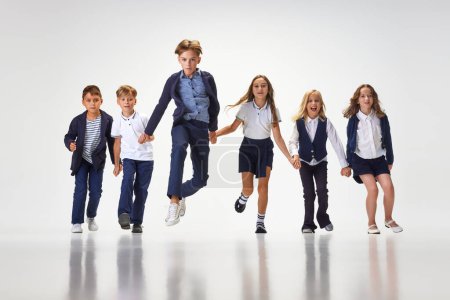 Photo for Group of stylish children, boys and girls, pupils in school uniform running against white studio background. Classmates. Concept of childhood, school, education, fashion, style. Copy space for ad - Royalty Free Image
