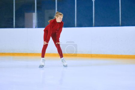 Foto de Chica en ropa deportiva roja, atleta de patinaje artístico de pie en la zona de pista de hielo y preparándose para la sesión de entrenamiento. Concepto de deporte profesional, competición, escuela de deporte, salud, hobby, anuncio - Imagen libre de derechos