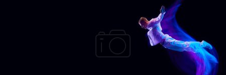 Photo for Freedom. Young guy in stylish clothes falling down over black studio background in neon with mixed lights effect. Concept of movements, art, dance and sport, fashion, youth. Banner. Copy space for ad - Royalty Free Image