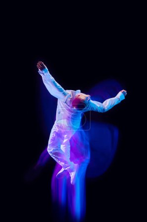 Photo for Freedom of movements. Young man in stylish clothes in motion against black studio background in neon with mixed lights effect. Concept of movements, art, dance and sport, fashion, youth, ad - Royalty Free Image