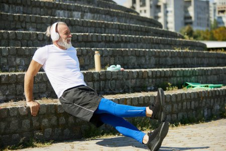 Foto de Musculoso, hombre mayor en entrenamiento de ropa deportiva al aire libre, haciendo ejercicios de flexiones inversas en las escaleras. Concepto de estilo de vida activo y deportivo, edad, cuidado de la salud, ejercicio, vitalidad, ad - Imagen libre de derechos