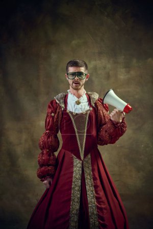 Photo for Young guy in image of medieval royal person wearing female dress standing with megaphone against vintage background. Concept of historical retrospectives, fashion, provoking projects, gender fluidity - Royalty Free Image