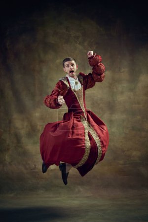 Photo for Young emotional man, medieval royal person, prince emotionally jumping in female dress against vintage background. Concept of historical retrospectives, fashion, provoking projects, gender fluidity - Royalty Free Image