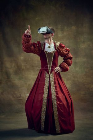 Photo for Historical education. Royal man, medieval prince in female dress wearing vr glasses over vintage green background. Concept of historical retrospectives, fashion, provoking projects, modern technology - Royalty Free Image