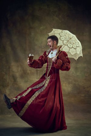Photo for Joyful man, medieval prince walking in female dress with umbrella and drinking beer against vintage background. Concept of historical retrospectives, fashion, provoking projects, gender fluidity - Royalty Free Image