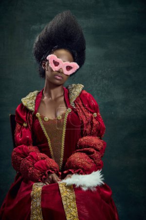 Photo for Looking at world through pink glasses. Young african woman, princess wearing elegant red dress and sunglasses against vintage background. Concept of history, beauty and fashion, comparison of eras, ad - Royalty Free Image