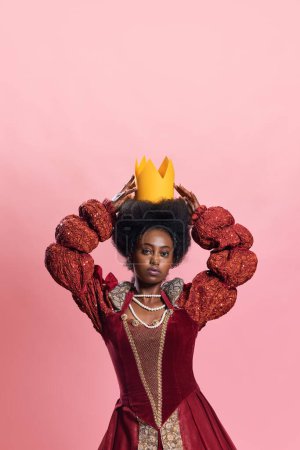Photo for Royal Elegance. Portrait of young, beautiful african woman, medieval princess in vintage dress with paper crown against pink background. Concept of history, beauty and fashion, comparison of eras, ad - Royalty Free Image