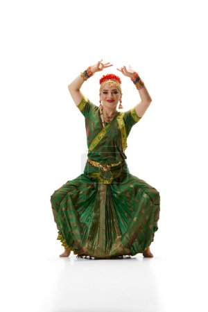 Foto de Elegancia de la danza tradicional india. Hermosa mujer en vestido verde haciendo rendimiento contra fondo de estudio blanco. Concepto de belleza, moda, India, tradiciones, estilo de vida, coreografía, arte. Anuncio - Imagen libre de derechos