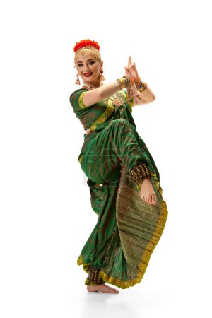 Foto de Hermosa mujer en vestido verde bailando la danza tradicional india bharatanatyam contra fondo de estudio blanco. Concepto de belleza, moda, India, tradiciones, estilo de vida, coreografía, arte. Anuncio - Imagen libre de derechos
