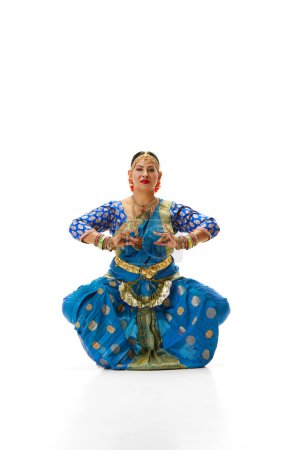 Foto de Hermosa mujer india madura en vestido tradicional bailando danza india contra fondo de estudio blanco. Concepto de belleza, moda, India, tradiciones, estilo de vida, coreografía, arte. Anuncio - Imagen libre de derechos