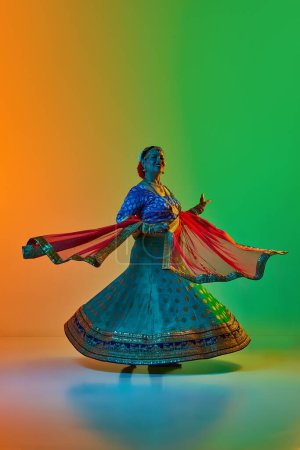 Photo for Beautiful, smiling, mature indian woman in traditional indian dress dancing against gradient studio background in neon light. Concept of beauty, fashion, India, traditions, choreography, art. Ad - Royalty Free Image