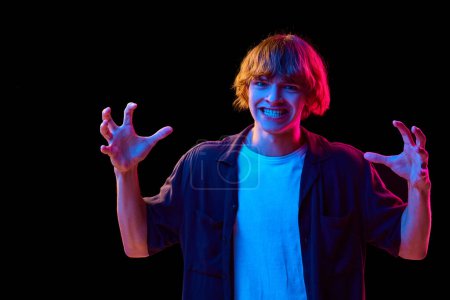 Photo for Portrait of young guy, student in casual clothes showing irritation and annoyance against black studio background in neon lights. Concept of human emotions, facial expression, youth, lifestyle. Ad - Royalty Free Image