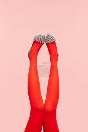 Foto de Aspecto elegante. Delgadas piernas femeninas en medias de color rojo brillante y zapatos de tacón con estilo sobre fondo rosa. Fotografía colorida. Concepto de moda, creatividad, imaginación. Copiar espacio para anuncio - Imagen libre de derechos