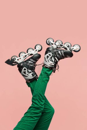 Foto de Patas femeninas con rodillos y pantalones verdes sobre fondo rosa. Estilo de vida activo y deporte. Fotografía colorida. Concepto de moda, creatividad, imaginación. Copiar espacio para anuncio - Imagen libre de derechos