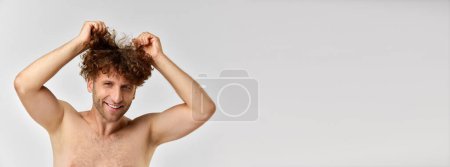 Photo for Messy hair. Positive mature man standing shirtless and taking care after curly hair against grey studio background. Concept of mens beauty, body and skin care, cosmetology, wellness. Banner, ad - Royalty Free Image