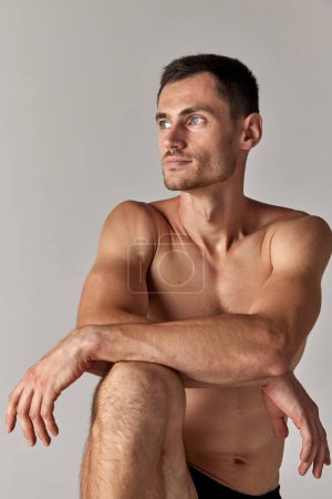 Téléchargez les photos : Portrait d'un beau jeune homme aux yeux gris, posant torse nu sur fond de studio gris. Corps musculaire. Concept de santé et de beauté masculine, soins du corps, fitness, bien-être, publicité - en image libre de droit