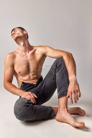 Téléchargez les photos : Homme au corps musclé, fort et en relief posant torse nu en jeans sur fond de studio gris. Bien-être. Concept de santé et de beauté masculine, soins du corps, fitness, bien-être, publicité - en image libre de droit