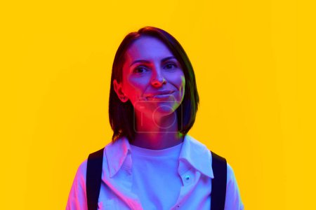 Photo for Portrait of elegant woman in her 30s wearing white shirt, looking with smile against orange studio background in neon light. Concept of human emotions, fashion, lifestyle, facial expression, ad - Royalty Free Image