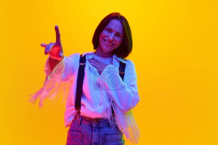 Photo for Happy, smiling woman in her 30s wearing white shirt and suspenders against orange studio background in neon light. Concept of human emotions, fashion, lifestyle, facial expression, ad - Royalty Free Image