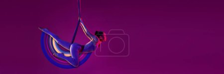 Foto de Joven chica flexible haciendo yoga aéreo, entrenamiento sobre fondo púrpura en luz de neón con elementos de diseño abstractos. collage de arte contemporáneo. Concepto de deporte, creatividad, acción y movimiento, salud - Imagen libre de derechos