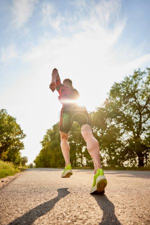 Photo for Back view dynamic image of sportsman, runner in sportswear training, running alone the road. Concept of professional sport, triathlon preparation, competition, athleticism - Royalty Free Image
