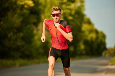 Photo for Speed and endurance. Motivated sportsman in sportswear running along the road, training outdoors. Concept of professional sport, triathlon preparation, competition, athleticism - Royalty Free Image