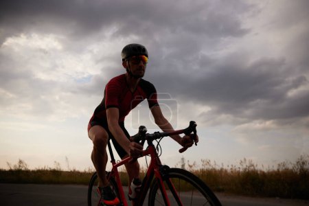 Téléchargez les photos : Homme compétitif, triathlète à vélo sur route à l'extérieur, entraînement pour le marathon. Concept de sport professionnel, préparation au triathlon, compétition, athlétisme - en image libre de droit