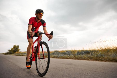 Téléchargez les photos : Homme compétitif et motivé, triathlète à vélo sur route à l'extérieur, entraînement pour le marathon. Concept de sport professionnel, préparation au triathlon, compétition, athlétisme - en image libre de droit