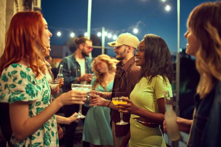 Photo for Young beautiful people, friends meeting in evening on rooftop, cheerfully talking, drinking cocktails. Concept of party, leisure time, fun and joy, weekends, celebration, youth culture - Royalty Free Image