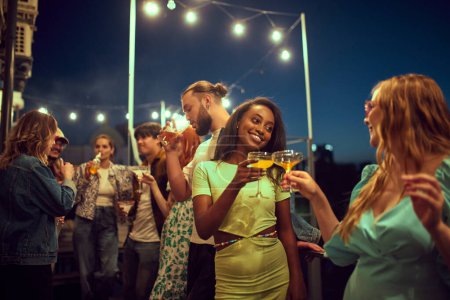 Photo for Stylish young people, friends meeting in evening outdoors, on rooftop, drinking, talking, having fun together. Concept of party, leisure time, fun and joy, weekends, celebration, youth culture - Royalty Free Image