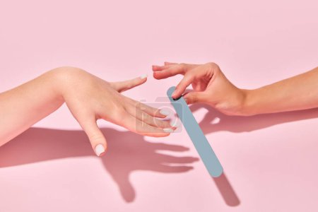 Photo for Female hand with nail file taking care after hands, nails against pink background. Elegant natural look. Concept of hand care, cosmetics and cosmetology, spa, natural beauty. Poster, ad - Royalty Free Image