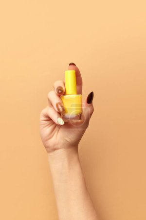 Téléchargez les photos : Femme main tenant vernis à ongles sur fond beige. Manucure pastel multicolore. Concept de soins des mains, cosmétiques et cosmétologie, spa, beauté naturelle. Affiche, annonce - en image libre de droit