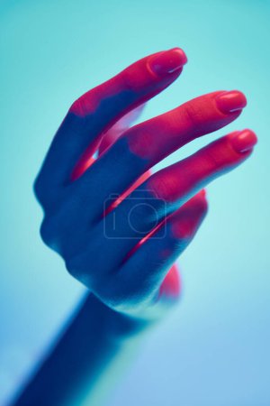 Téléchargez les photos : Belle main féminine bien entretenue isolée sur fond bleu sous la lumière du néon. Ongles naturels, nus, manucure. Concept de soins des mains, cosmétiques et cosmétologie, spa, beauté naturelle. Affiche, annonce - en image libre de droit
