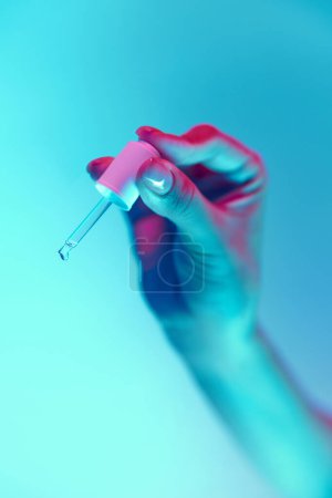 Photo for Well-kept female hand with nude, natural nails, manicure holding nail polish, top gel isolated over blue background in neon light. Concept of hand care, cosmetics and cosmetology, beauty. Poster, ad - Royalty Free Image