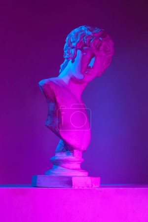 Foto de Arte griego. busto estatua antigua contra fondo púrpura estudio en luces de neón. Copia de yeso. Concepto de estilo antiguo, arte clásico, museo, historia y mitología. Póster, anuncio - Imagen libre de derechos