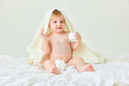 Photo for After shower body care. Little girl, toddler sitting in bed in towel and holing moisturizing cream. Concept of childhood, kids cosmetology and natural cosmetics, body care - Royalty Free Image