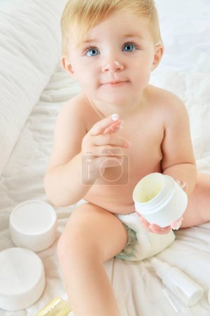 Photo for Cute, beautiful child, little baby girl with cream on nose and finger, in diaper in bed at home. Skincare products. Concept of childhood, kids cosmetology and natural cosmetics, body care - Royalty Free Image