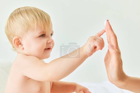 Photo for Tender touch. Little baby girl, child sitting in bed, toughing mothers finger with cream. Beauty products for babies. Concept of childhood, kids cosmetology and natural cosmetics, body care - Royalty Free Image