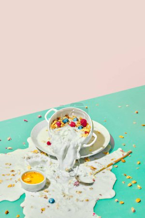 Foto de Derramando leche en la mesa. Cuenco con cereales, muesli con bayas y leche sobre fondo pastel. El desayuno. Concepto de comida saludable, nutrición, estilo pop art, sabor. Cartel. Copiar espacio para anuncio - Imagen libre de derechos
