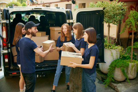 Photo for Group of young people, man and women, volunteers loading many boxes of humanitarian goods into van. Concept of humanitarian aid, assistance and support, care, social programs - Royalty Free Image