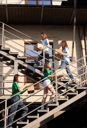 Photo for Girls, volunteers standing on stairs with boxes filled with humanitarian help, clothes, goods, food and meds. Concept of humanitarian aid, assistance and support, care, social programs - Royalty Free Image