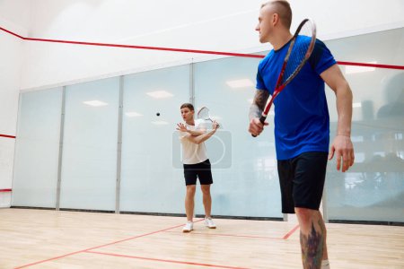 Téléchargez les photos : Deux jeunes hommes, des amis jouant au squash ensemble sur le terrain de squash. Concurrence et loisirs. Concept de sport, passe-temps, mode de vie sain et actif, jeu, gymnase, publicité - en image libre de droit