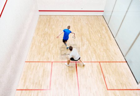Foto de Vista superior de dos jóvenes, amigos, deportistas jugando squash en la cancha de squash. Competencia. Concepto de deporte, hobby, estilo de vida saludable y activo, juego, gimnasio, anuncio - Imagen libre de derechos