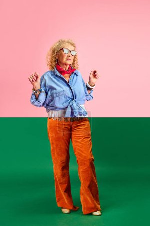 Foto de Collage hecho de mitades de imágenes de mujer mayor en diferentes ropas elegantes de pie sobre fondo rosa verde. Diversidad. Concepto de emociones, moda, personas mayores, estilo de vida, creatividad. Anuncio - Imagen libre de derechos