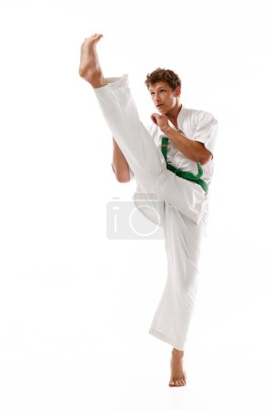 Foto de Imagen dinámica del joven en entrenamiento de kimono blanco aislado sobre fondo de estudio blanco. Karate, taekwondo, atleta de judo. Concepto de artes marciales, deporte de combate, energía, fuerza, salud. Anuncio - Imagen libre de derechos