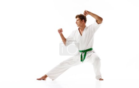 Photo for Young guy, karate sportsman in white kimono and green belt standing in pose to fight isolated on white studio background. Concept of martial arts, combat sport, energy, strength, health. Ad - Royalty Free Image