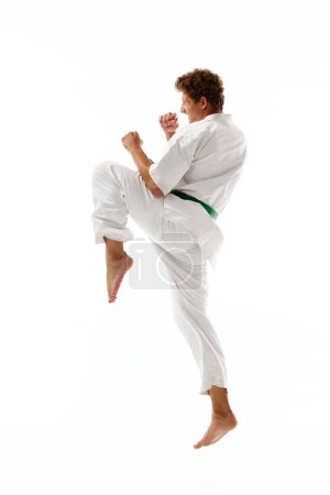 Photo for Athletic young man, karateka in white kimono and green belt training, practicing karate isolated on white studio background. Concept of martial arts, combat sport, energy, strength, health. Ad - Royalty Free Image
