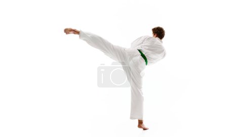 Photo for Side view of young man, karate, taekwondo athlete in kimono and green belt training isolated on white studio background. Concept of martial arts, combat sport, energy, strength, health. Ad - Royalty Free Image