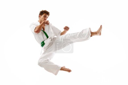 Foto de Patada en un salto. Hombre atlético joven, karateka en entrenamiento en movimiento, practicando aislado en el fondo blanco del estudio. Concepto de artes marciales, deporte de combate, energía, fuerza, salud. Anuncio - Imagen libre de derechos